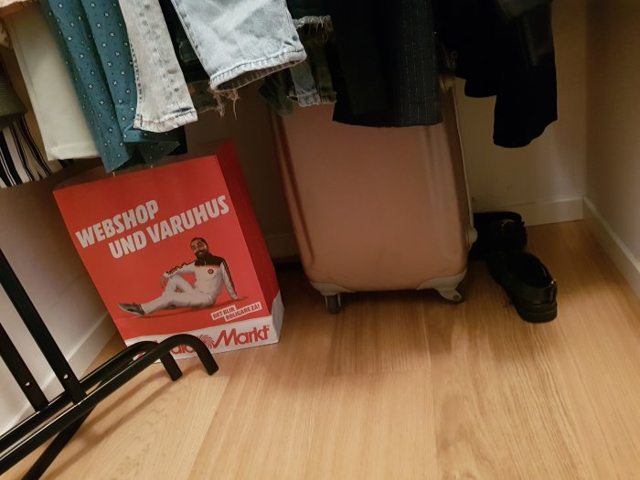 Del av en walk-in closet med klädhängare, en resväska och en sko på golvet.