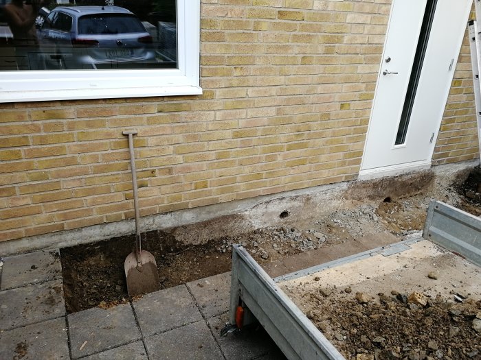 Grävningsarbete framför hus med synliga borrhål i betongplattan och terrakottarör delvis synligt.