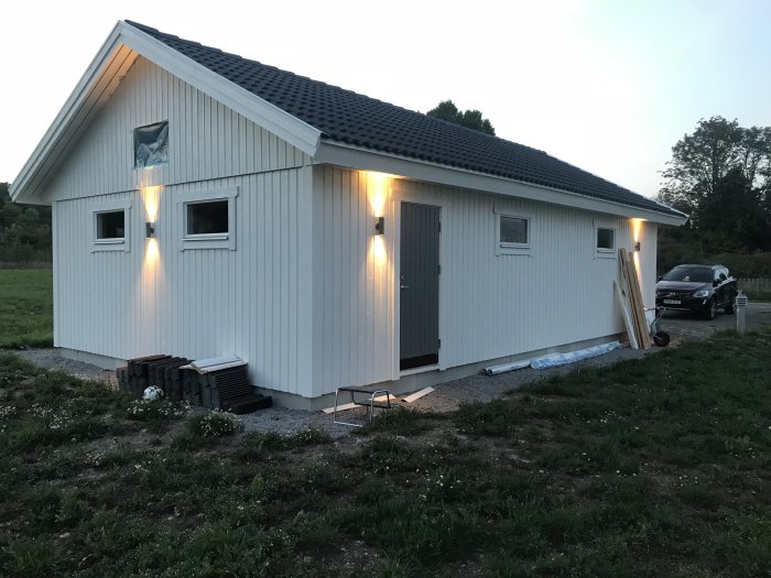 Nybyggt hus i skymningen med exteriörbelysning tänd och en bil parkerad utanför.