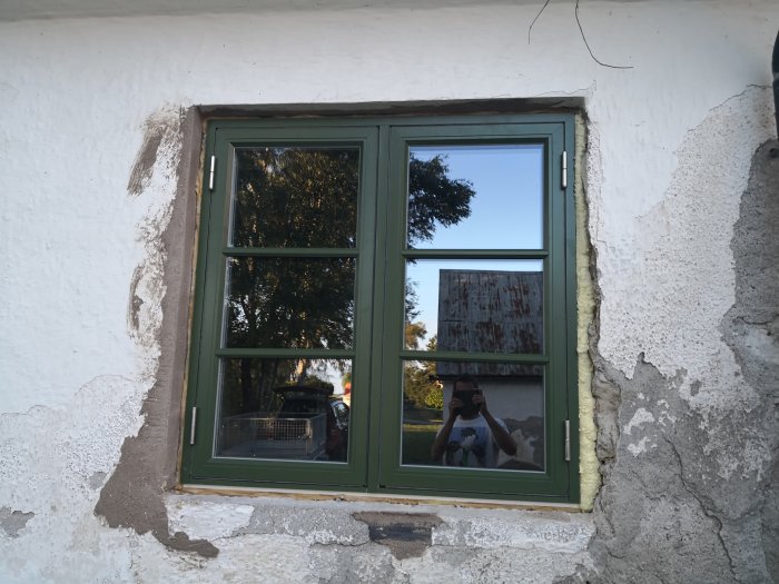 Grönt fönster med färgkod S6020-G30Y installerat i vit putsad vägg, omgiven av oslipad puts.