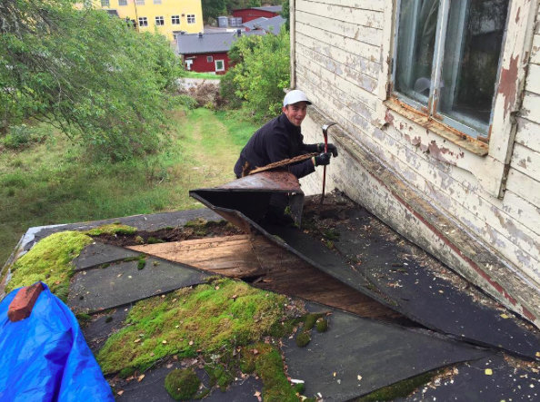 Man river gammalt skadat plåttak på husutbyggnad med synlig mossa och fuktighet.