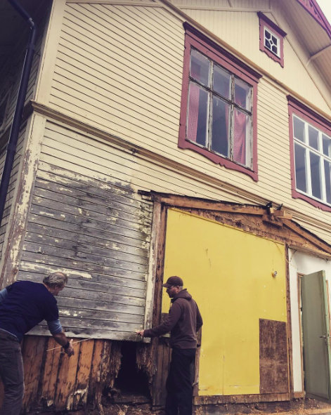 Två personer demonterar skadat innertak på gammal utbyggnad av hus med synliga fuktskador.