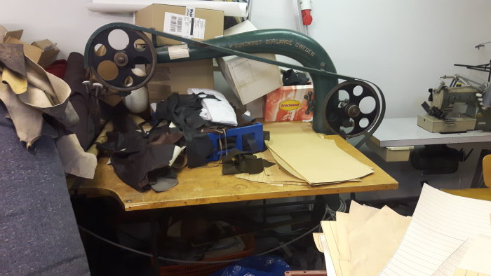 Bandsåg omgiven av textilrester och mönsterpapper i en verkstad.