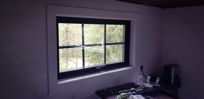 Interiör utsikt från ett vardagsrum genom ett nyinstallerat fönster med skogsbakgrund.