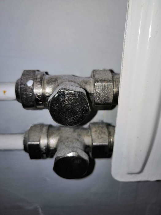 Närbild av radiatoranslutning med synliga rör och kopplingar mot väggen.