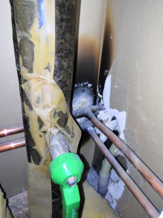 Röranslutning vid vägg med kopparledningar och öppen servicelucka, eventuellt för radiatoravstängning.