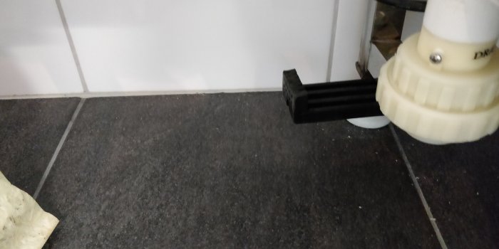 Svarta L-formade justerbara fötter från ett massagebadkar nära vit badrumsvägg och klinkergolv.