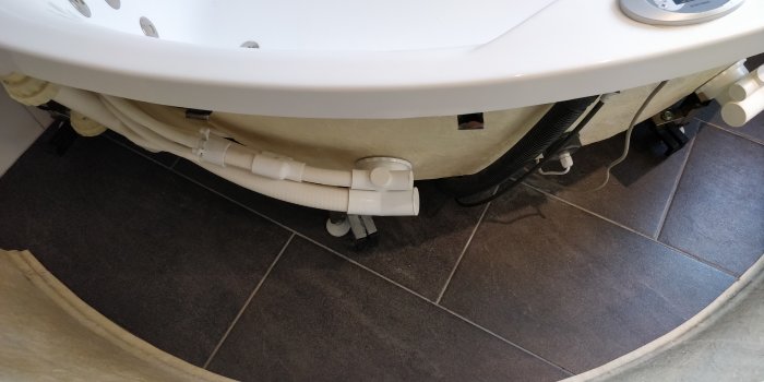 Öppet undersida av ett vit Camargue Alicante massagebadkar som visar rörledningar och svarta L-formade fästen.