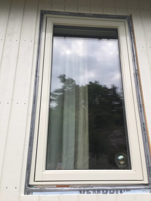 Nyinstallerat fönster med synlig isolering och vindskydd, monterat i en vit vägg.