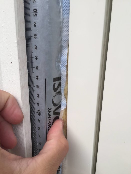 Mätning av isolering vid altandörr med linjal, vindskydd syns i nivå med aluminiumkant.