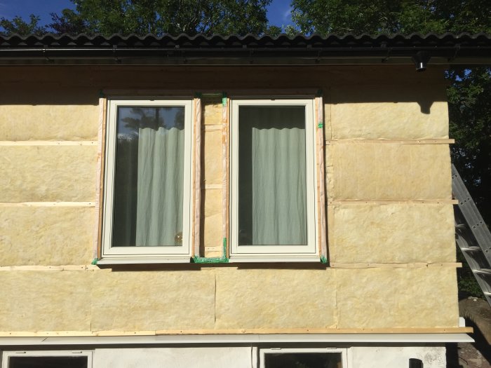 Två installerade fönster på ett hus under renovering med tilläggsisolering och skyddande vindduk.