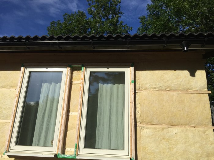 Nyinstallerade fönster med tilläggsisolering och vindduk på en husvägg under renovering.