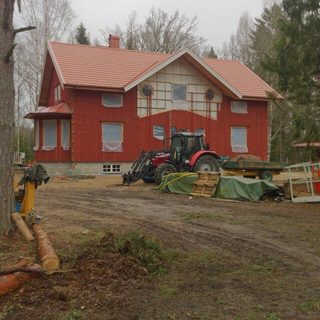 Rödmålat hus under konstruktion med synliga byggmaterial och traktor i förgrunden.