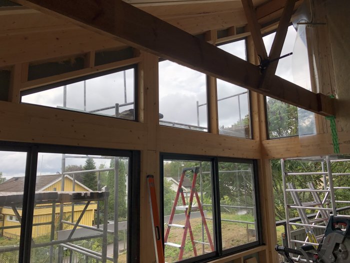 Träkonstruktion och fönster av ett hus under renovering med stege i bakgrunden.
