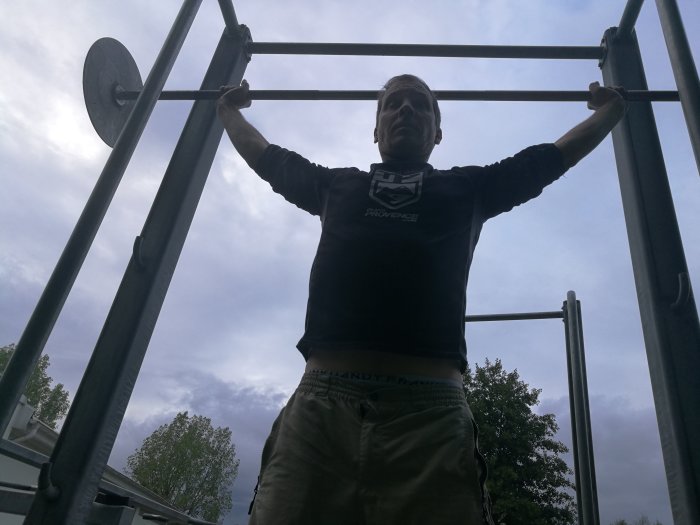 Person utför styrketräning utomhus genom att lyfta en viktskivstång i ett lyftstativ.