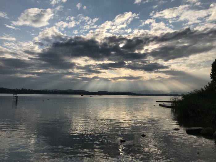 Solstrålar som bryter igenom molnen över Lago di Varese i Italien efter regnväder.