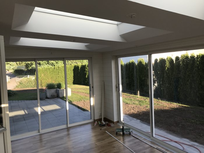 Interiör av ett nybyggt uterum med ekparkett och stora fönster mot en trädgård.