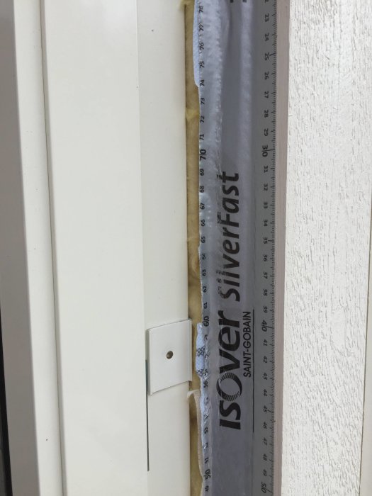 Borttagna aluminiumprofiler vid en fönsterkarm som avslöjar en 15 mm springa med isolering och vindduk.