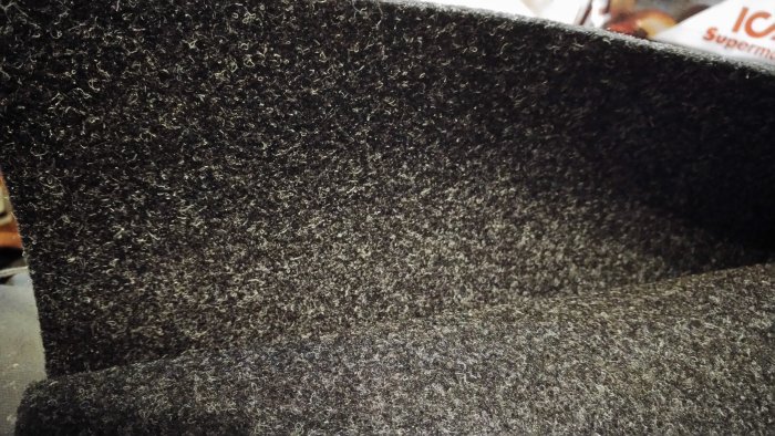 Närbild på en grå filtmatta med synligt slitage och viss trådbildning, indikerande ålder och användning.