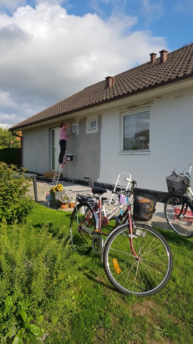 Person på stege som målar ett hus med cyklar i förgrunden.