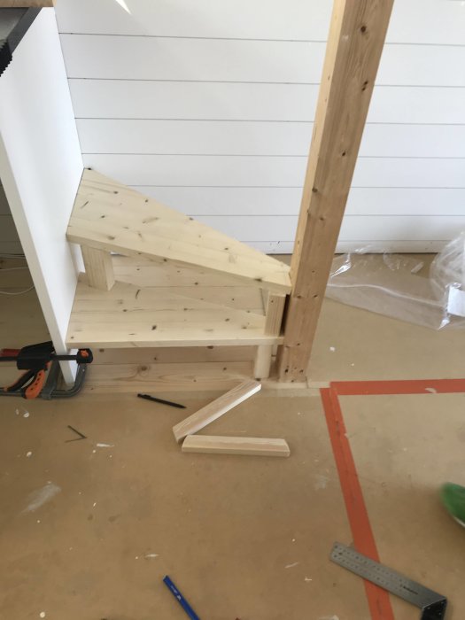 En delvis konstruerad träspiraltrappa inuti en vitpanelad sjöbod under uppbyggnad.