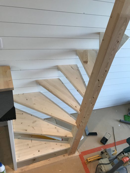 Konstruktion av en träspiraltrappa med verktyg och byggmaterial synliga runtomkring.