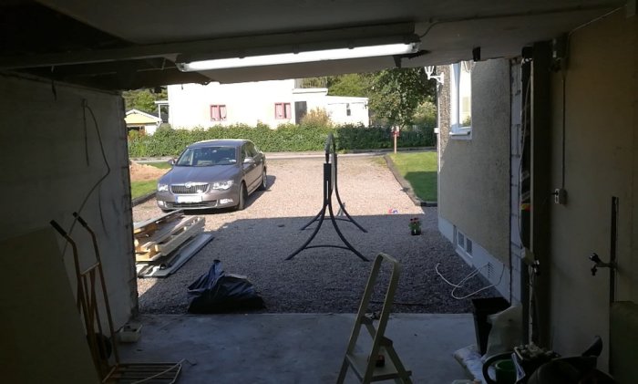 Vy inifrån garage med orenoverad vägg och utsikt till en bil parkerad utomhus.