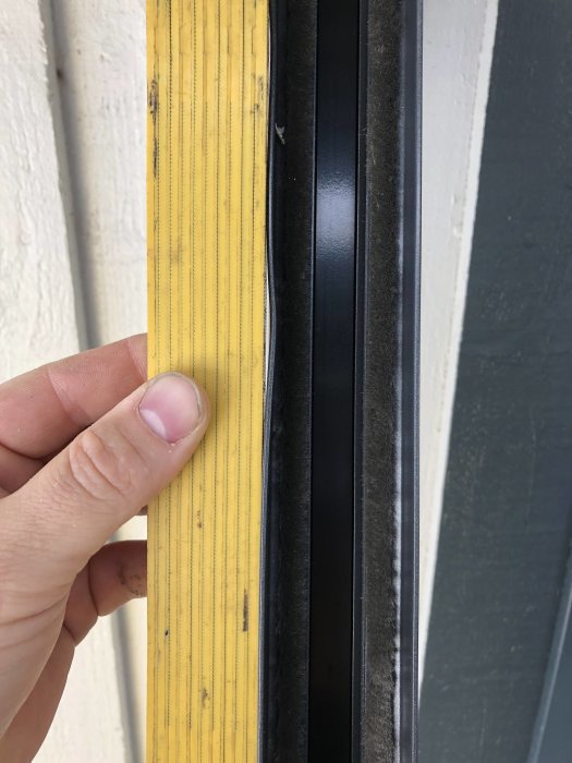 Närbild av en hand som håller i en skadad gult profilerad dörrlist intill en svart skjutdörrskarm.