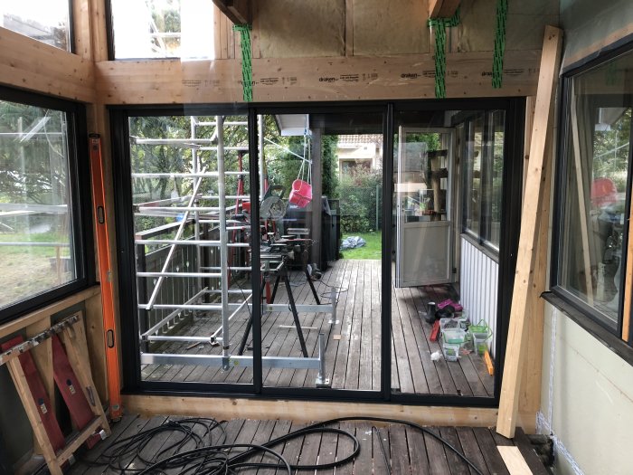 Nyinstallerade skjutdörrar mot en altan, synliga byggmaterial och verktyg, med trädgården i bakgrunden.