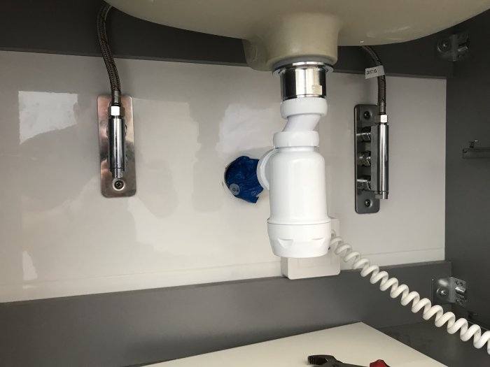 Moderna avloppsanslutningar och flexibla slangar dragna genom golvet under handfatet.