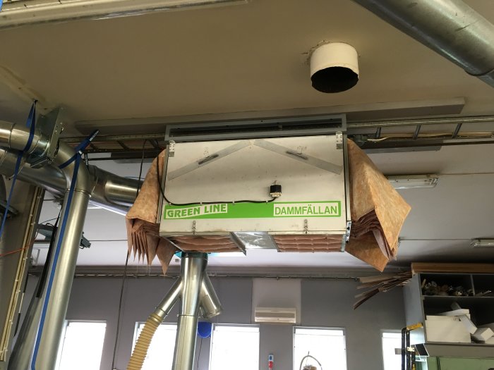 Ett upphängt luftreningsfilter i ett verkstadsutrymme, fastsatt nära taket med spännband.
