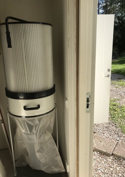Spånsug placerad i ett förråd, synlig genom en öppen dörr, med fokus på behållare och filter.
