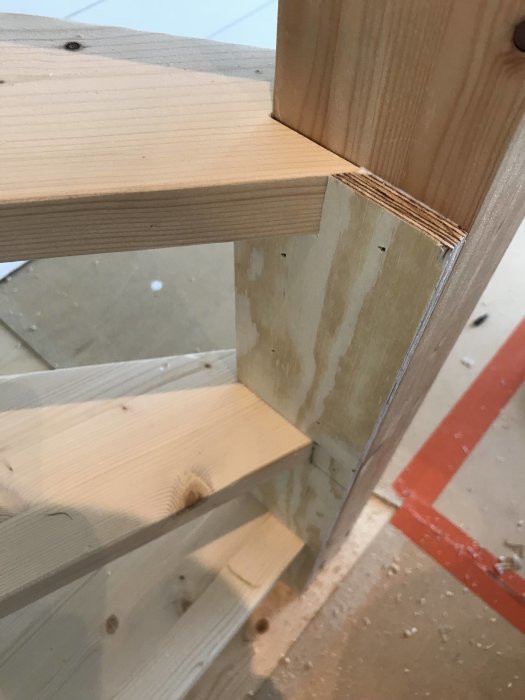 Detaljbild av pågående trappbygge med ofärdiga trästeg och stolpe, förarbete inför klädsel och målning.