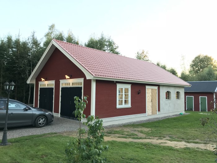 Ett nästan färdigt rött garage med tjockputsade lecaväggar, svarta garageportar, och 20-talslampor.