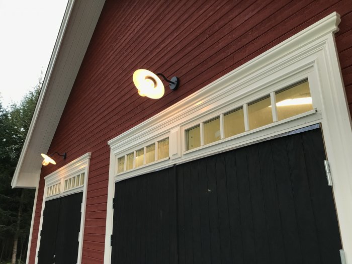 Nästan färdigt garage med rödmålad puts, svarta portar, överljus och tjugotalslampor.