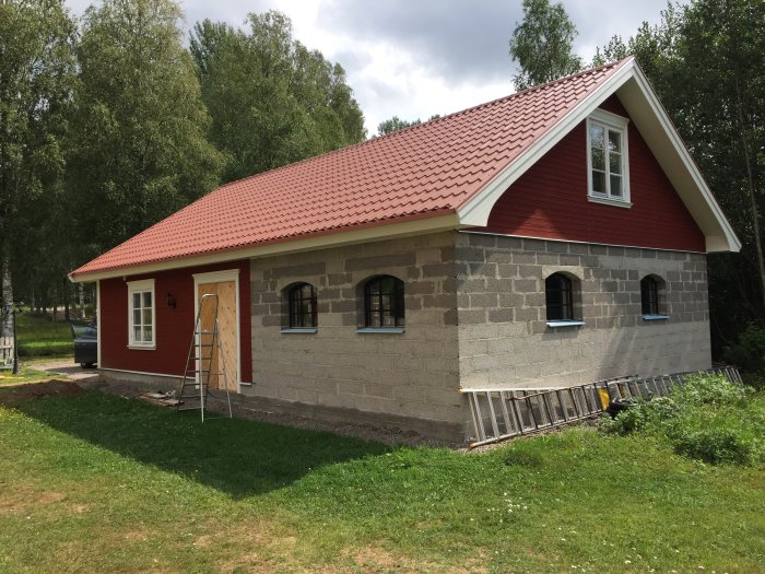 Rödputsat garage med lecaväggar och tegeltak, fönster monterade, utan hängrännor och målning.