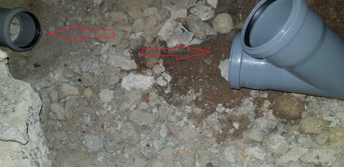 Avloppsrör i betonggolv med utmanande vinkel, röda pilar indikerar kopplingsbehov.