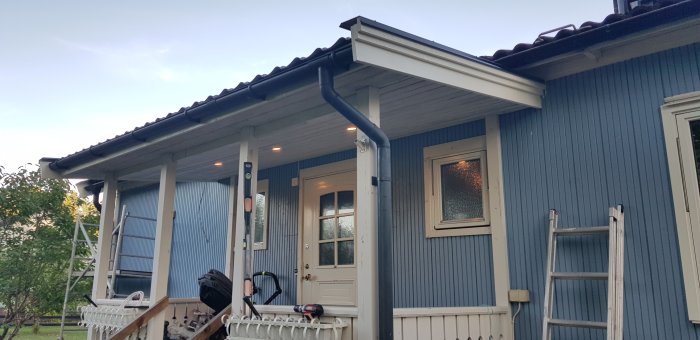 Renoverad entré med nya vindskivor och takfotsbräda på ett blått hus, stege lutad mot huset.