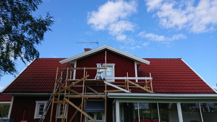 Renoverat trähus med nytt vindskivebyte, ställningar runt fasaden och klarblå himmel i bakgrunden.