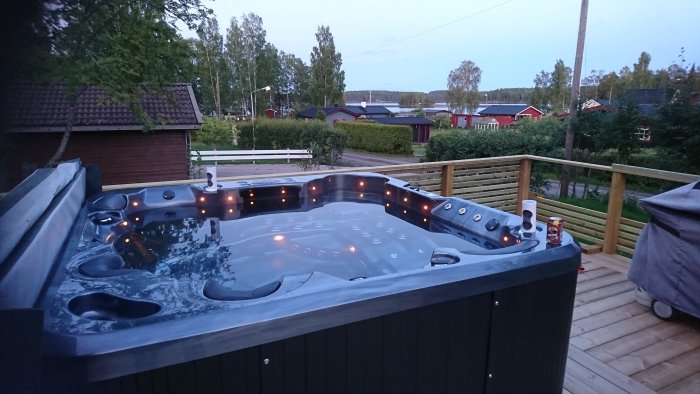 Ett jacuzzi-spa installerat på en träterrass med bostäder i bakgrunden vid skymning.