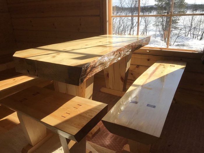 Handgjort bord och bänkar av finsk gran och furu i solbelyst rum med snöutsikt.