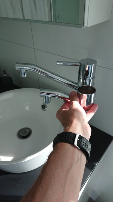 Hand håller en ny kranpip bredvid monterad badrumskran för jämförelse av längden.