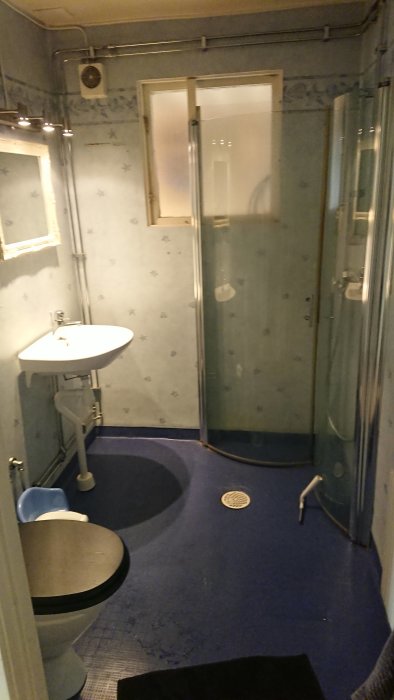 Gammalt badrum med handfat, toalett och glasdusch, redo för rivning och renovering.