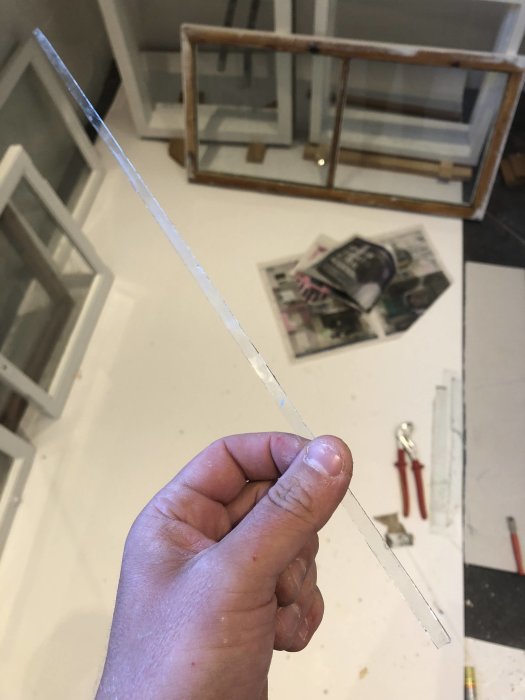 Nyss tillskuret smalt fönsterglas hållet av en person med verktyg och fönsterbågar i bakgrunden.