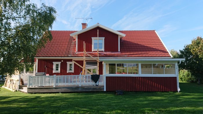 Röd villa med avlägsnad byggställning visar altantakets två sektioner, plast över fönstret för målning.