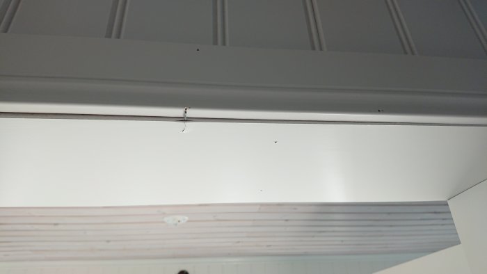 Taklister mot ett vitmålat träpaneltak med synligt lim och en liten glipa.