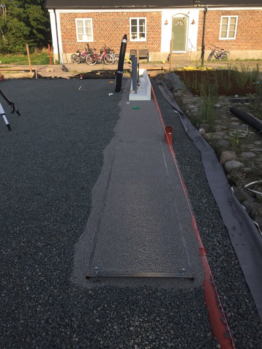 Justerbara avdragsbanor installerade på ett grusunderlag för exakt nivellering vid läggning av marksten.