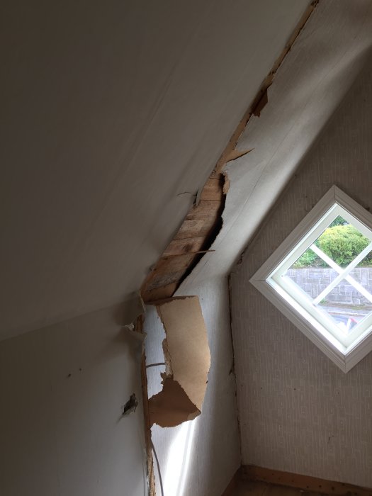 Skadat snedtak med synlig råspont och bortfallande ytskikt i ett äldre trähus.