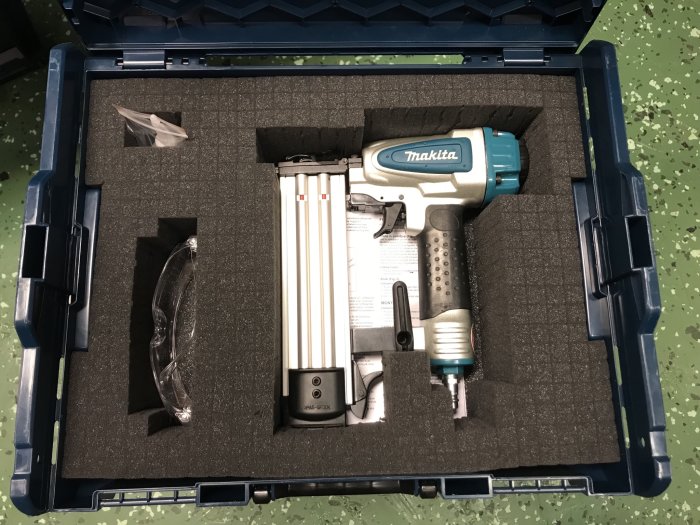 Makita af505n spikpistol i öppen väska med närliggande tillbehör och bruksanvisning.