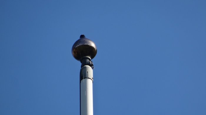 Topp av en 11 meters flaggstång med ny flagglina fästad mot en klarblå himmel.